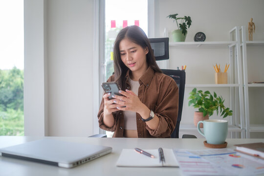 Smiling businesswoman checking messages on her smartphone while standing in a bright modern office.