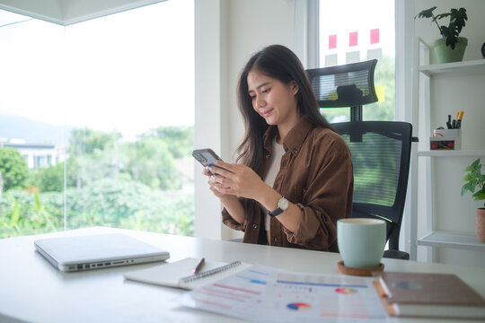 Smiling businesswoman checking messages on her smartphone while standing in a bright modern office.