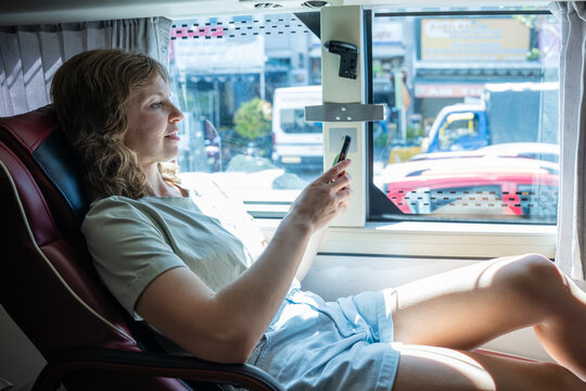 Woman using smartphone while sitting in comfortable sleeper bus seat during long distance travel in Southeast Asia