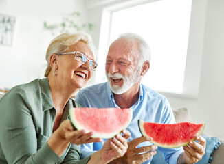 Portrait of a happy senior couple embracing eating watermelon  and having fun at home