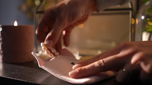 Woman's hands opening a small pink pouch and taking out a beautiful pearl and silver bracelet. Cozy atmosphere with a candle burning in the background
