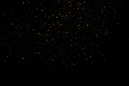 Shimmering gold flakes, sparkling gold particles on a black background. Tiny material for backgrounds or textures in art designs.