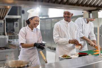 Group of chefs smiling and working together in professional kitchen, preparing, plating dishes with...