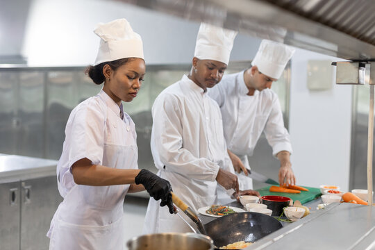 Group of chefs smiling and working together in professional kitchen, preparing, plating dishes with joy. Great for concepts like culinary teamwork, chef training, kitchen lifestyle restaurant culture.