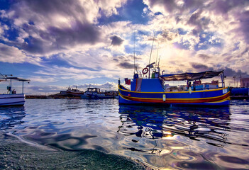 Marsaxlokk, Malta &ndash; Scenic harbor scene with fishing boat, water reflections and atmospheric sky lighting
