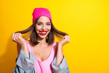 Naklejka premium Young woman in pink beanie smiling with playful hair pull urban fashion vibe on vibrant yellow background
