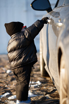 Child playing outdoors in winter sun. A young child stands confidently in a winter outfit, enjoying the sunlight on a chilly day near parked cars.