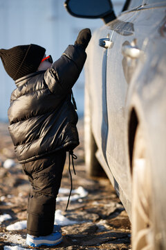 Child playing outdoors in winter sun. A young child stands confidently in a winter outfit, enjoying the sunlight on a chilly day near parked cars.