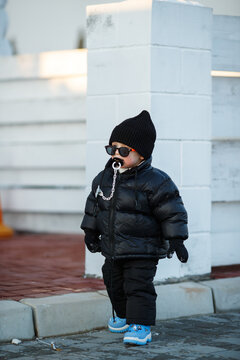 Joyful curious and independent toddler kid walks along the path in the winter forest. A little boy in warm overalls and a hat enjoys a walk in the winter snowy forest during winter holidays.