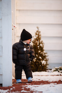 Joyful curious and independent toddler kid walks along the path in the winter forest. A little boy in warm overalls and a hat enjoys a walk in the winter snowy forest during winter holidays.