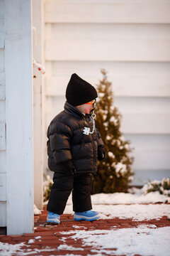 Joyful curious and independent toddler kid walks along the path in the winter forest. A little boy in warm overalls and a hat enjoys a walk in the winter snowy forest during winter holidays.