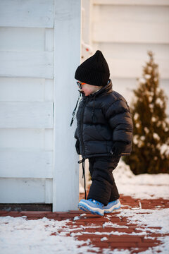 Joyful curious and independent toddler kid walks along the path in the winter forest. A little boy in warm overalls and a hat enjoys a walk in the winter snowy forest during winter holidays.