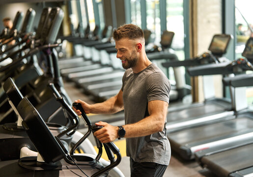 Portrait of a young man exercising on an elliptical trainer in a gym, running using  thereadmill machine equipment, healthy lifestyle and cardio exercise at fitness club concepts