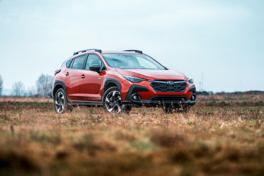 Brno, Czech Republic - February 15, 2025: Orange Subaru Crosstrek crossover stands outdoors in nature on a dirt road. Modern Japanese hybrid car.