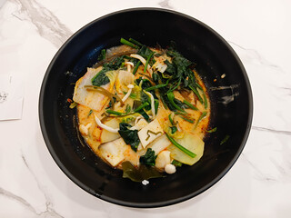 Spicy mala soup served in a black bowl, filled with vegetables and herbs, rich chili broth, hot flavor, Asian comfort food style.