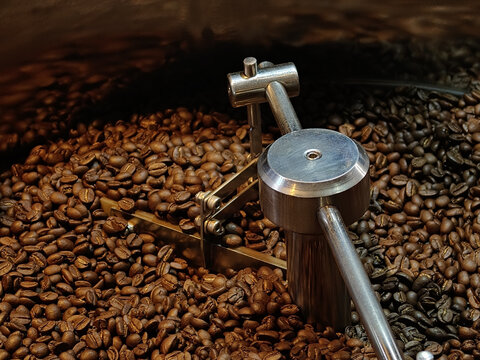 Freshly roasted coffee beans in roasting machine showcase rich textures and colors. metallic tool highlights roasting process, emphasizing craft of coffee making