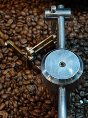 Freshly roasted coffee beans surround metallic coffee roasting machine, showcasing intricate design and craftsmanship involved coffee preparation. rich aroma of coffee fills air, inviting