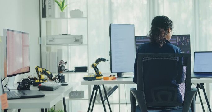 Young African American female robotics engineer coding AI software for robotic arm in laboratory. Embedded system, firmware testing, machine learning, industrial automation, future technology concept.