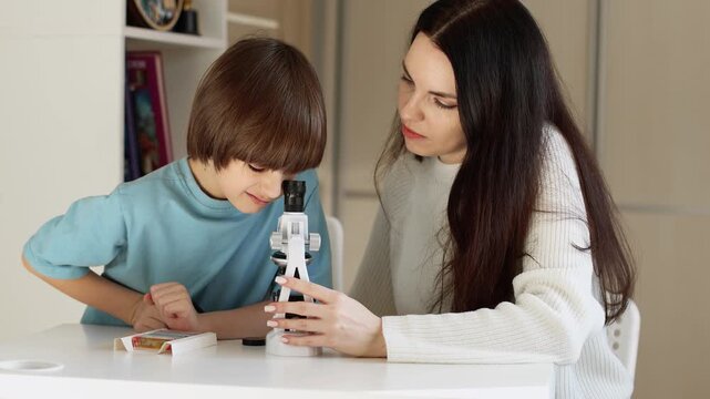 4K slow motion video of a mother helping her young son use a microscope at home. Child learning science with parent support, early education, curiosity, homeschooling, family educational activity.