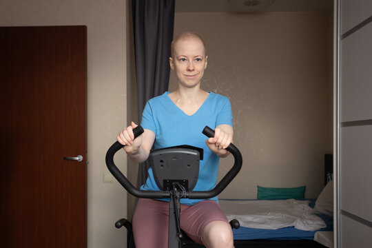 Adult oncology patient in sportswear using exercise bike in cozy bedroom, home rehab program after hospital discharge, maintaining physical activity and strength during cancer therapy