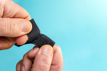 Obraz premium Velcro fastener tape with hook and loop tape openeb by male fingers on blue background, soft focus close up