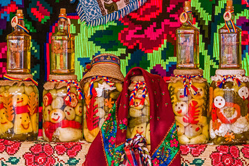 Fototapeta premium Jars with pickles and bottles with alcohol, traditional from area Maramures, Romania, displayed on a background with traditional embroidery.