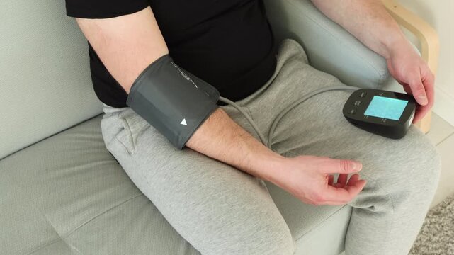 Man using an automatic digital blood pressure monitor at home for personal health self-check