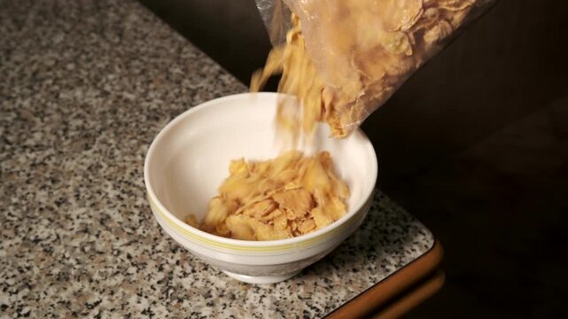 Person pouring cornflake cereal into a white bowl