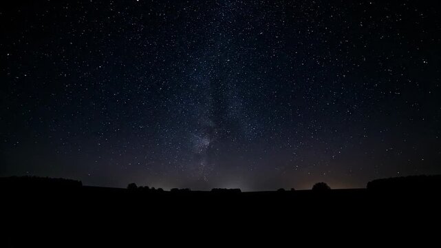Peaceful twilight view of a dark field silhouette under a deep blue starry sky, ideal for space exploration themes or serene background visuals.