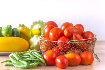 Various fresh vegetables: tomatoes, green beans, cucumbers, cabbage on a woodent table agaisnt white background; copy space