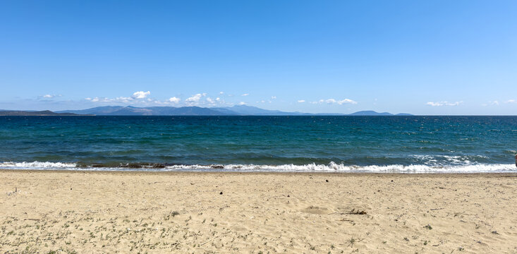 Sunny seascape from Marathon beach near Athens, Greece. Gentle waves on a sandy shore and distant mountains, blue sky