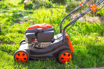 An orange and black lawn mower sits on a lush green lawn in the bright sun, ready to mow the grass