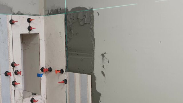 Worker Laying Ceramic Tiles on the Wall. Repairman Placing White Gray Square Tiles, Applying Adhesive. Builder Installing Tile Using Leveler, Tile Leveling Clips. Tiling. Finishing Repair Work. 4K