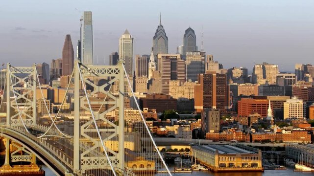 Aerial view of Philadelphia's skyline during golden hour, featuring modern skyscrapers and historic buildings. The calm river in the foreground creates a peaceful ambiance.