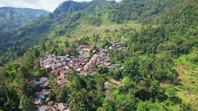 Aerial drone footage of Cisolok traditional village, with many thatch roof houses, metallic roof houses, gardens, green forests, and valleymountains behind, in Sukabumi regency,Java island, Indonesia
