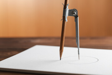 Composition with paper and drawing compass on wooden table. Drafting tool for geometry education and planning design.