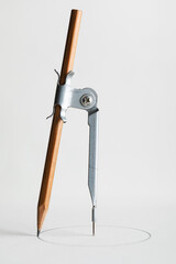 Drafting compass drawing circle on white paper background closeup.