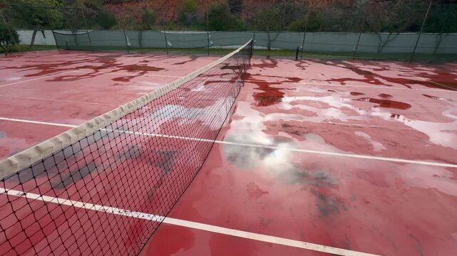 Wet clay tennis court with puddles during the rain. Outdoor tennis season. Spring rain on courts. All practices and match are cancelled