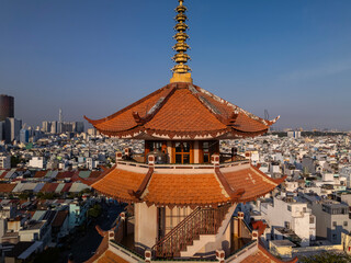 Buddhist Pagoda prayer tower in dense urban area in clear sunny late afternoon light. Rooftop, penthouse, spire and view of city skyline.