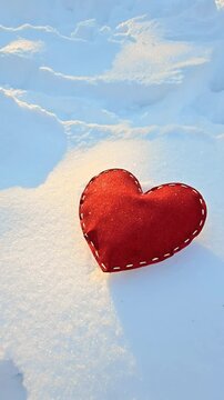 A shiny, stitched heart lies on the white snow on a frosty winter day. Vertical video