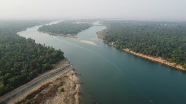Aerial drone view of the Nuanai River winding through dense forest landscape in Odisha, India. Wide river channel surrounded by green trees and natural riverbanks, captured in daylight from above. Sce