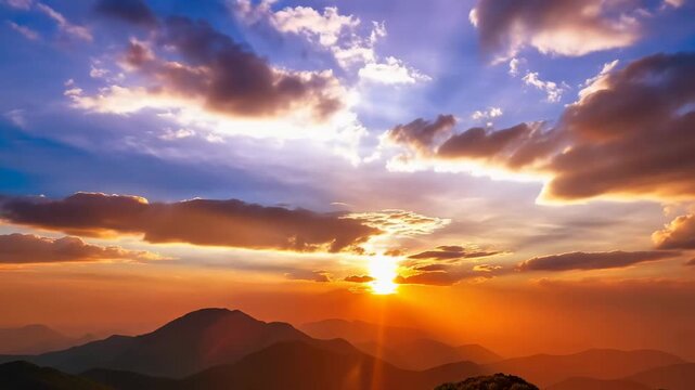 Sun rays break through clouds as the sun sets behind a mountain range. The sky changes colors during this beautiful evening display.