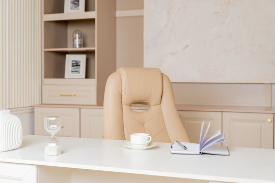 Elegant office desk table. Feminine workspace with paper notebook, cup of coffee, plant, chair. Luxury office interior in pastel colors.