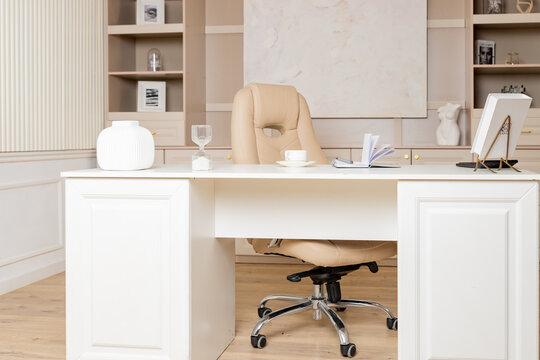 Elegant office desk table. Feminine workspace with paper notebook, cup of coffee, plant, chair. Luxury office interior in pastel colors.