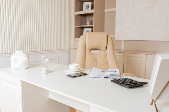 Elegant office desk table. Feminine workspace with paper notebook, cup of coffee, plant, chair. Luxury office interior in pastel colors.