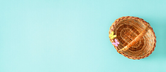 Empty wicker basket with decorative butterflies on blue background. Easter basket. Minimalistic spring flat lay layout. Banner.