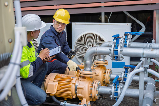 Two professional engineers inspecting industrial air conditioning system outside. Construction workers checking hvac maintenance with clipboard and toolbox at manufacturing factory site plant.