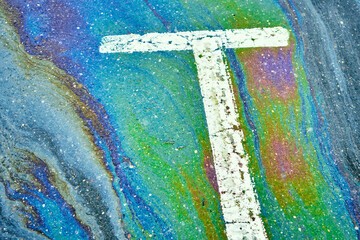 Oil slick on asphalt creating an iridescent, colorful, abstract pattern with a white line