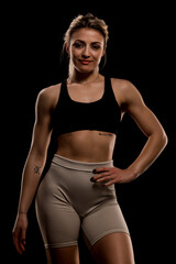 Obraz premium Confident woman in sporty attire posing against a dark background, showcasing fitness and strength in a low-light setting
