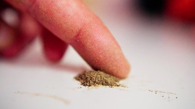 Person Carefully Tests Seasoning With Fingertip. Detailed Closeup Showing Finger Assessing Spice Texture. Individual Gently Touching Ground Spice Powder On Neutral Backdrop With Soft Lighting
